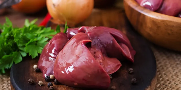 Fígado de boi cru com temperos, cebolas e ervas frescas sobre uma superfície de madeira.