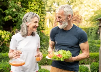Casal sênior sorridente ao ar livre com suco natural e prato de salada fresca