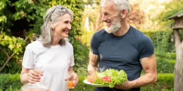 Casal sênior sorridente ao ar livre com suco natural e prato de salada fresca