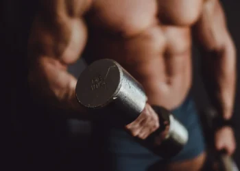 Homem musculoso segurando halter de 10 kg durante treino de braço.