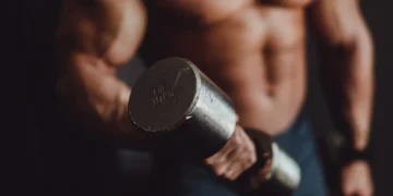 Homem musculoso segurando halter de 10 kg durante treino de braço.