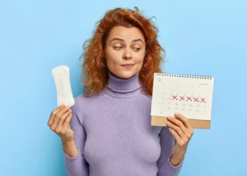 mulher segurando absorvente e calendário com marcações do ciclo menstrual.
