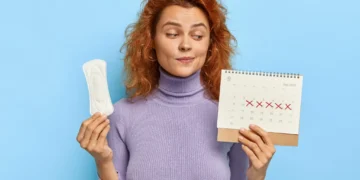 mulher segurando absorvente e calendário com marcações do ciclo menstrual.
