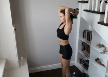 Mulher realizando exercício de tríceps com halteres em casa