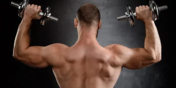 Homem forte levantando halteres, com foco no treino de força.