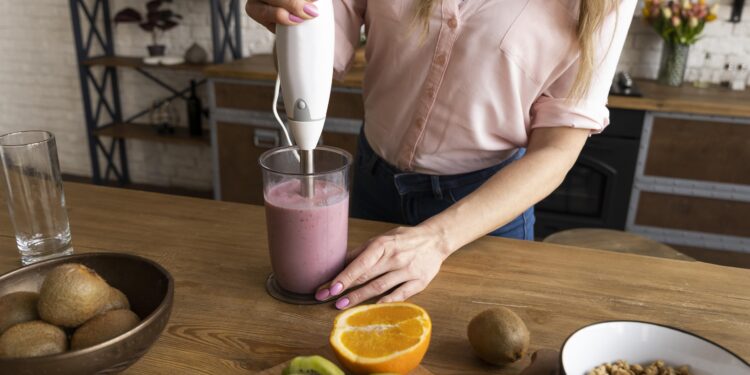 Mulher preparando vitamina de frutas com um mixer em um ambiente de cozinha rústica.