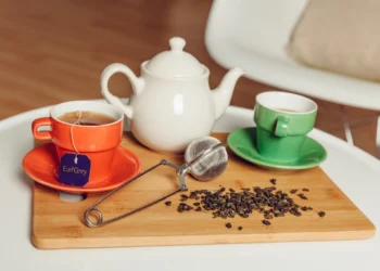 Xícara de chá Earl Grey ao lado de uma cafeteira e folhas de chá em uma tábua de madeira, representando a escolha entre café e chá.