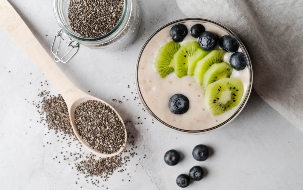 Colher com sementes de chia ao lado de pote de chia e tigela com smoothie de kiwi e mirtilo