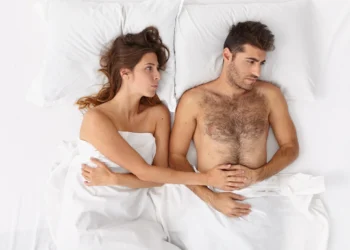 Casal deitado na cama, com expressões de desconexão emocional, representando um tema sobre o apetite sexual.