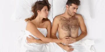 Casal deitado na cama, com expressões de desconexão emocional, representando um tema sobre o apetite sexual.