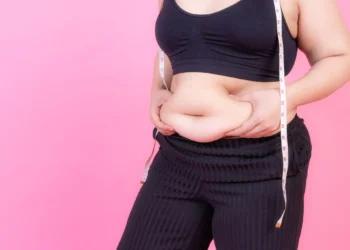 Mulher apertando a gordura abdominal com uma fita métrica, simbolizando a preocupação com a redução da gordura na barriga.