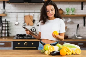 Mulher segurando uma laranja e usando um tablet enquanto prepara frutas na cozinha