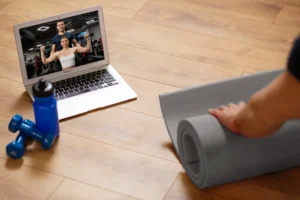 Pessoa preparando o espaço para exercício em casa com tapete e laptop.