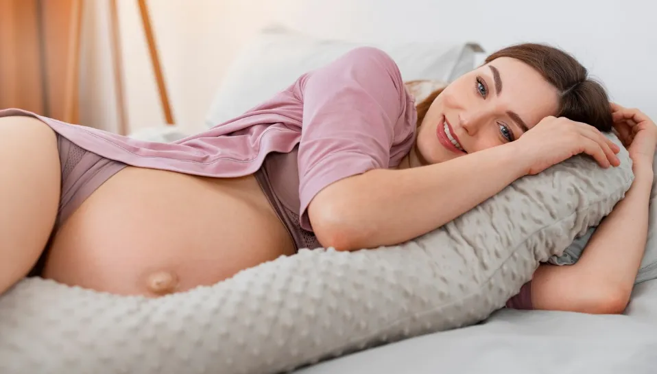 Mulher grávida deitada confortavelmente de lado com travesseiro de apoio, demonstrando postura ideal para gestantes.