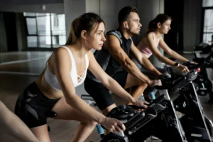 Pessoas concentradas praticando ciclismo indoor em academia para melhorar o condicionamento físico.