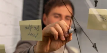 Pessoa desenhando mapa mental em vidro com caneta, com notas adesivas ao redor.