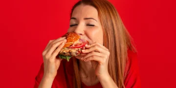 Mulher comendo hambúrguer, demonstrando a busca por prazer alimentar, mesmo após refeições.