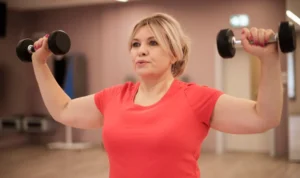 Mulher praticando musculação com halteres, exercitando os braços em ambiente de academia.