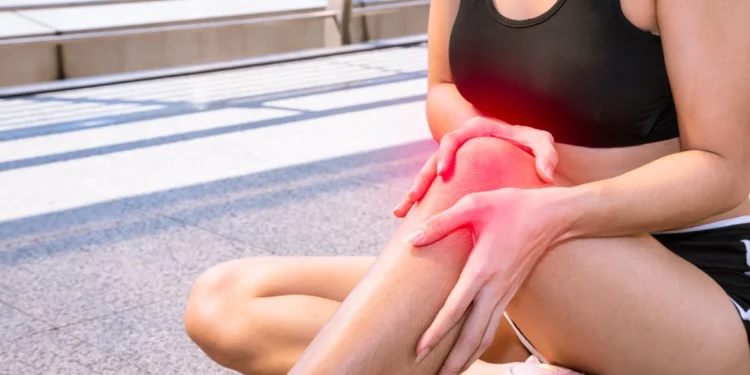 Mulher esportiva segurando o joelho com expressão de dor após exercício físico ao ar livre