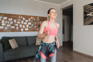 Mulher se exercitando em casa com roupas fitness, demonstrando alegria e saúde.