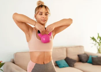 Mulher fazendo exercício de elevação com kettlebell para fortalecer braços e ombros em casa