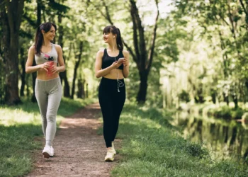 Duas mulheres caminhando em um parque verde, sorrindo e conversando durante uma caminhada ao ar livre.
