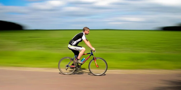Homem pedalando em alta velocidade em estrada rural com campos verdes ao fundo, simbolizando saúde e emagrecimento através do ciclismo.