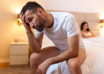 Homem com dificuldades na vida sexual sentado na cama, com expressão de preocupação.