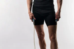 Homem atlético segurando corda de pular, destacando pernas e braços musculosos.