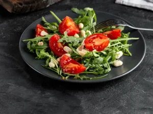 Salada fresca de rúcula com tomates e castanhas servida em prato preto