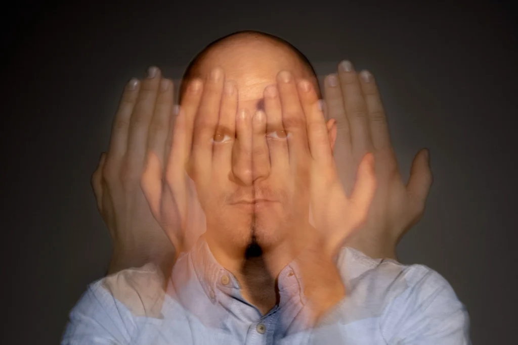 Homem com expressão séria cobrindo o rosto parcialmente com as mãos, representando sinais ocultos de esgotamento mental.