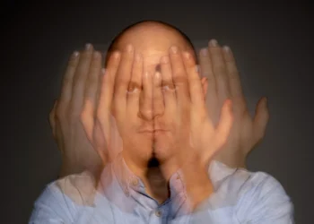 Homem com expressão séria cobrindo o rosto parcialmente com as mãos, representando sinais ocultos de esgotamento mental.