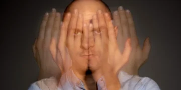 Homem com expressão séria cobrindo o rosto parcialmente com as mãos, representando sinais ocultos de esgotamento mental.