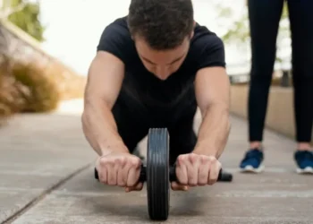 Homem utilizando roda abdominal durante treino ao ar livre com supervisão