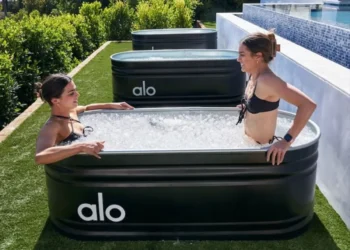 Duas pessoas fazendo banho de gelo após treino, relaxando em banheiras ao ar livre.