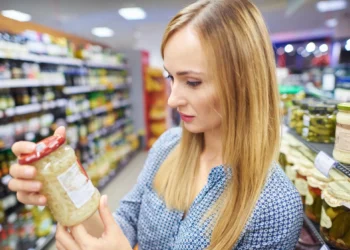 Mulher observando rótulo de produto alimentício em supermercado