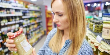 Mulher observando rótulo de produto alimentício em supermercado