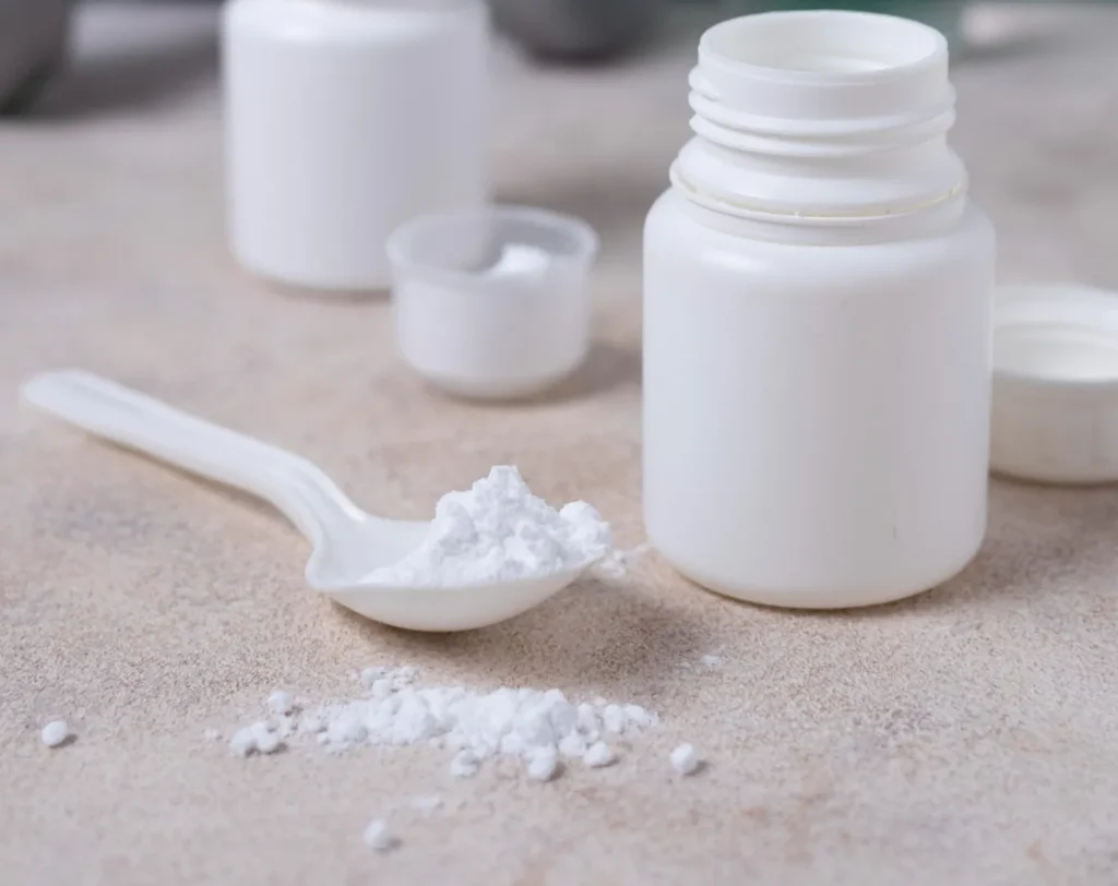 Pó de creatina em frascos com colheres, perto de halteres e água, ilustrando suplementos