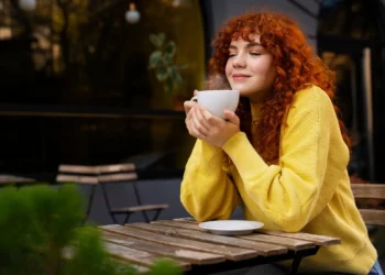 Mulher desfrutando de uma bebida quente no café, com um sorriso de prazer.