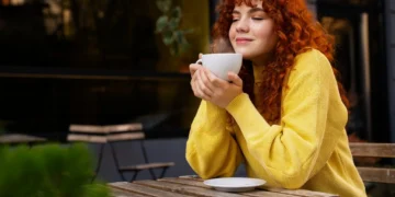 Mulher desfrutando de uma bebida quente no café, com um sorriso de prazer.