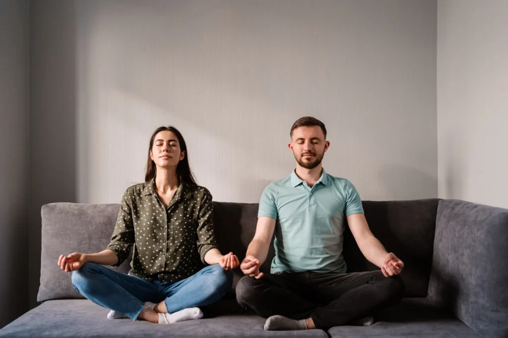 Casal sentado no sofá em posição de meditação para aliviar o estresse
