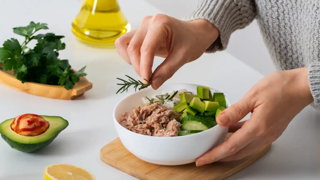 Tigela com atum, abacate e pepino sendo temperada com alecrim, alimentos fontes de ômega 3