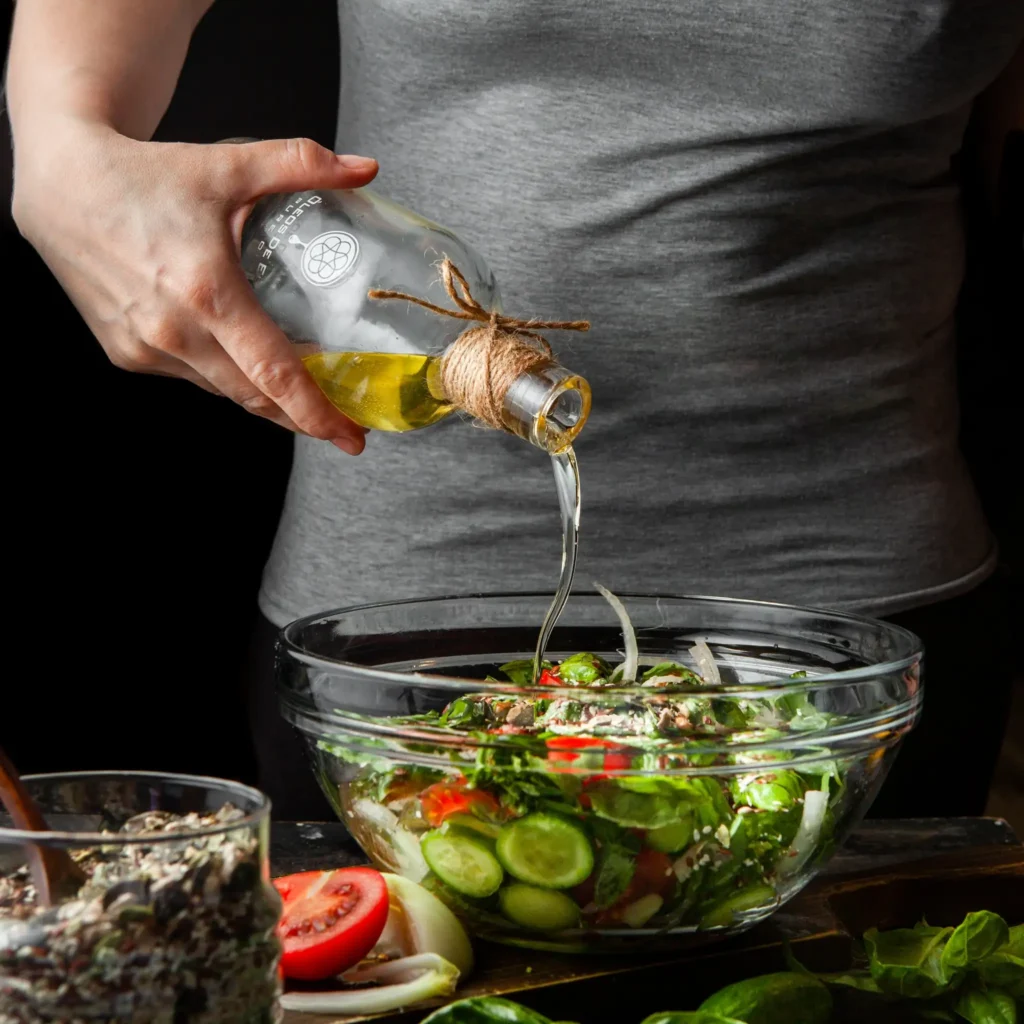 Mulher adicionando azeite de oliva a uma salada fresca, um exemplo prático de dieta mediterrânea.