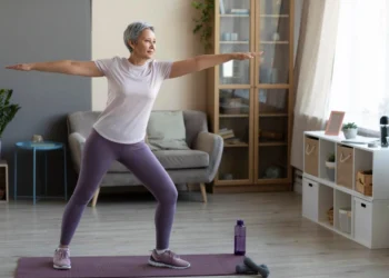 Mulher madura praticando yoga em casa, simbolizando a importância da atividade física na menopausa.