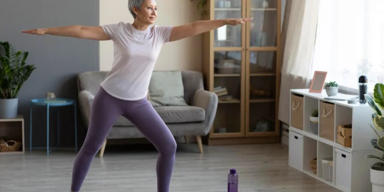 Mulher madura praticando yoga em casa, simbolizando a importância da atividade física na menopausa.