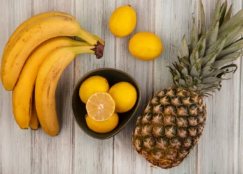 Bananas, limões e abacaxi dispostos sobre uma mesa de madeira clara