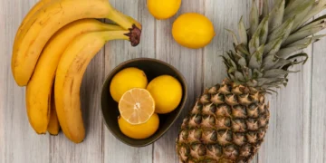 Bananas, limões e abacaxi dispostos sobre uma mesa de madeira clara
