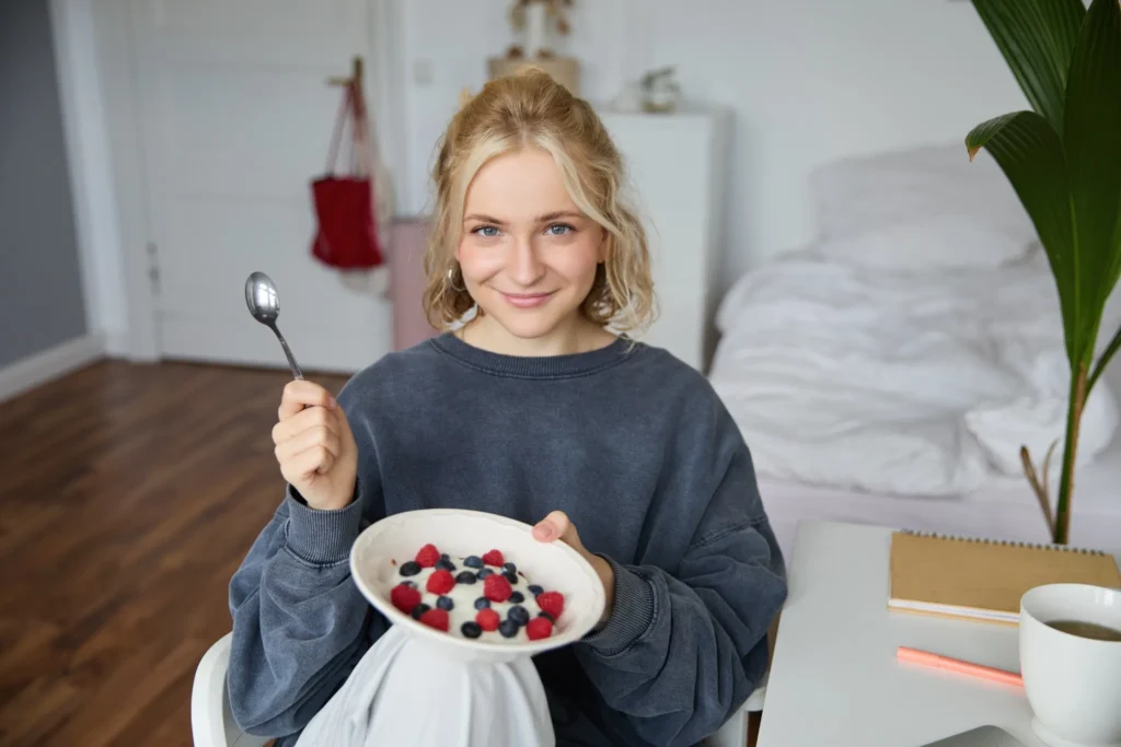 Mulher sorrindo enquanto segura uma tigela de iogurte com frutas vermelhas no café da manhã