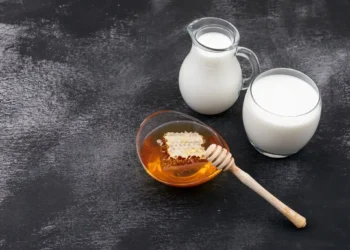 Imagem mostrando leite com mel, um remédio natural, em um fundo preto, destacando os benefícios para a saúde