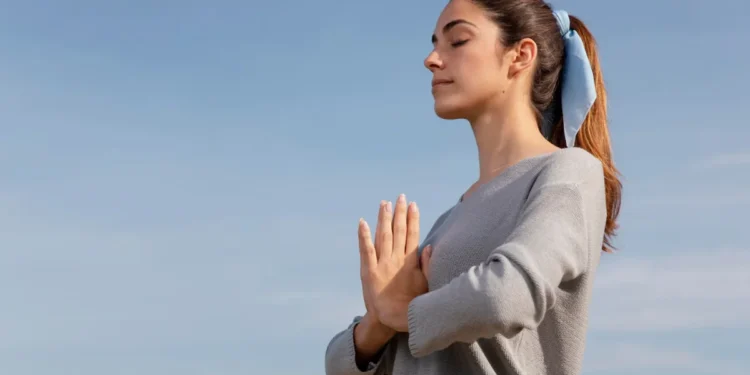 Mulher praticando respiração ao ar livre com expressão de tranquilidade